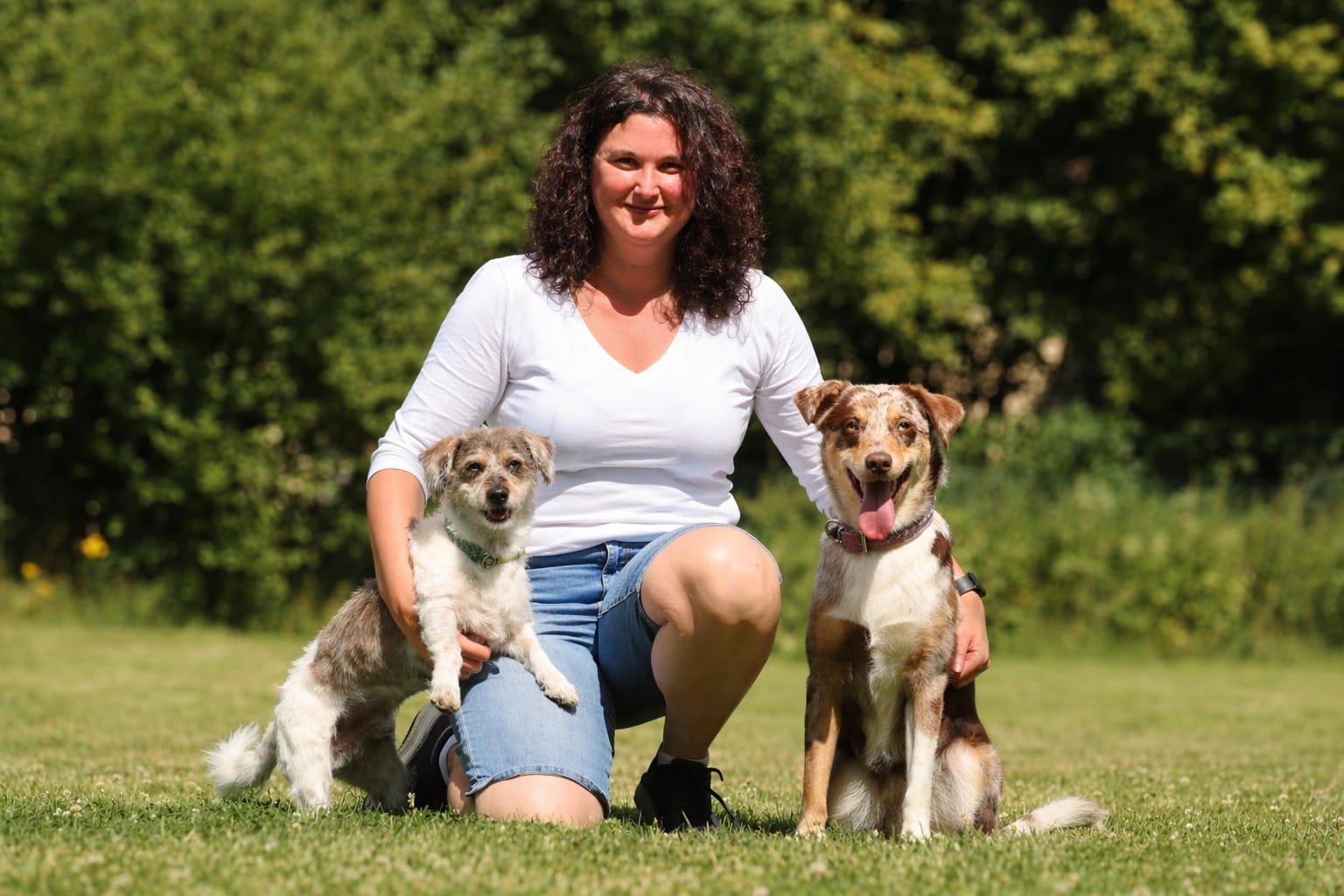 Lena Rummenholl kniet auf einer Wiese zwischen ihren Hunden Snickers und Lotti
